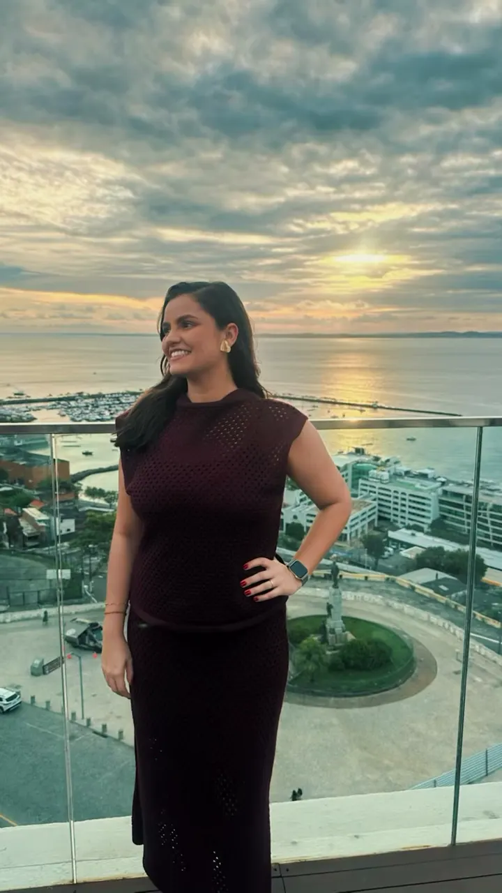 Mariana em uma varanda com a Baía de Todos os Santos ao pôr do sol